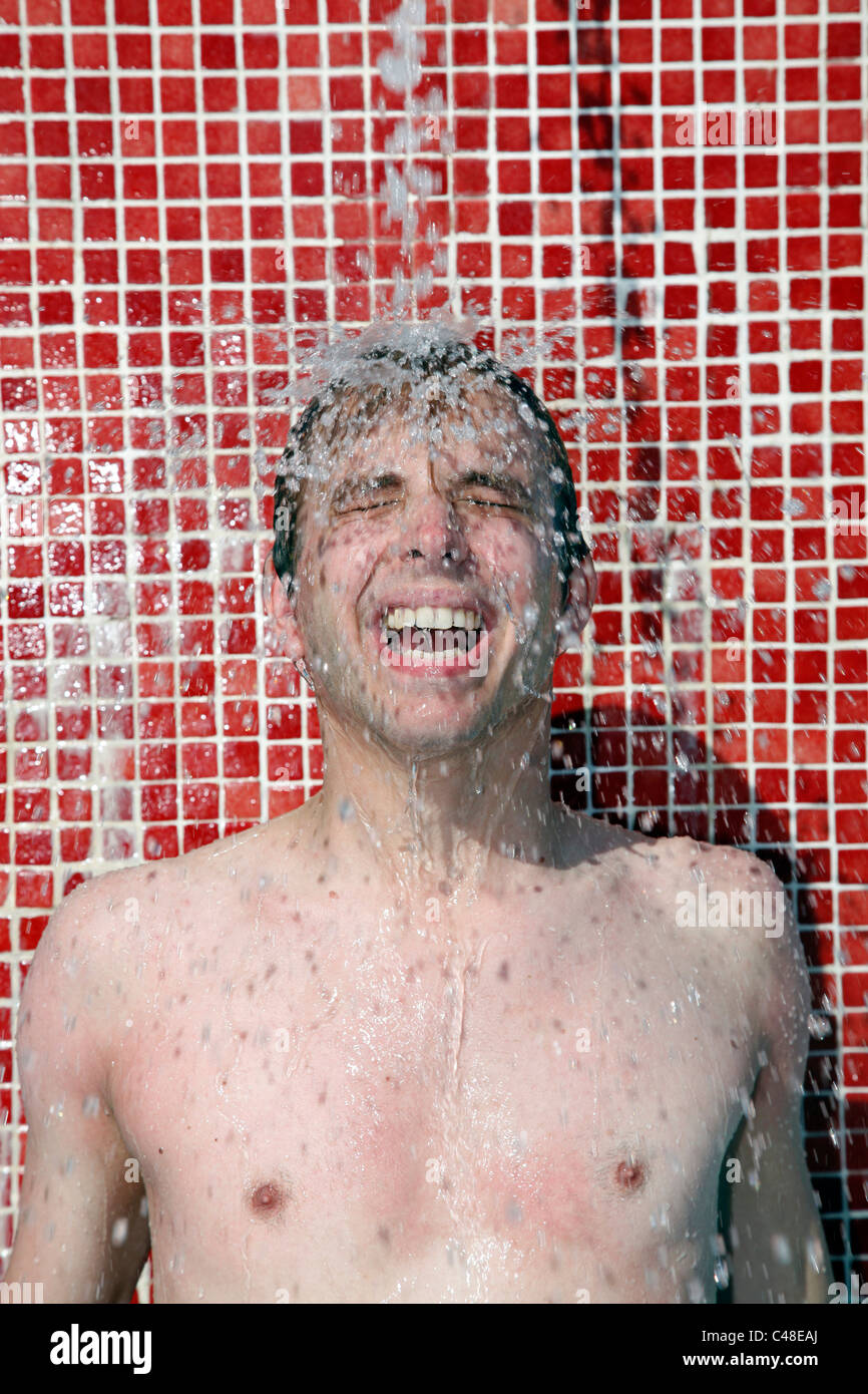 Parution du modèle homme sur des vacances lave ses cheveux sous la douche sur une plage avec les projections d'eau. Banque D'Images