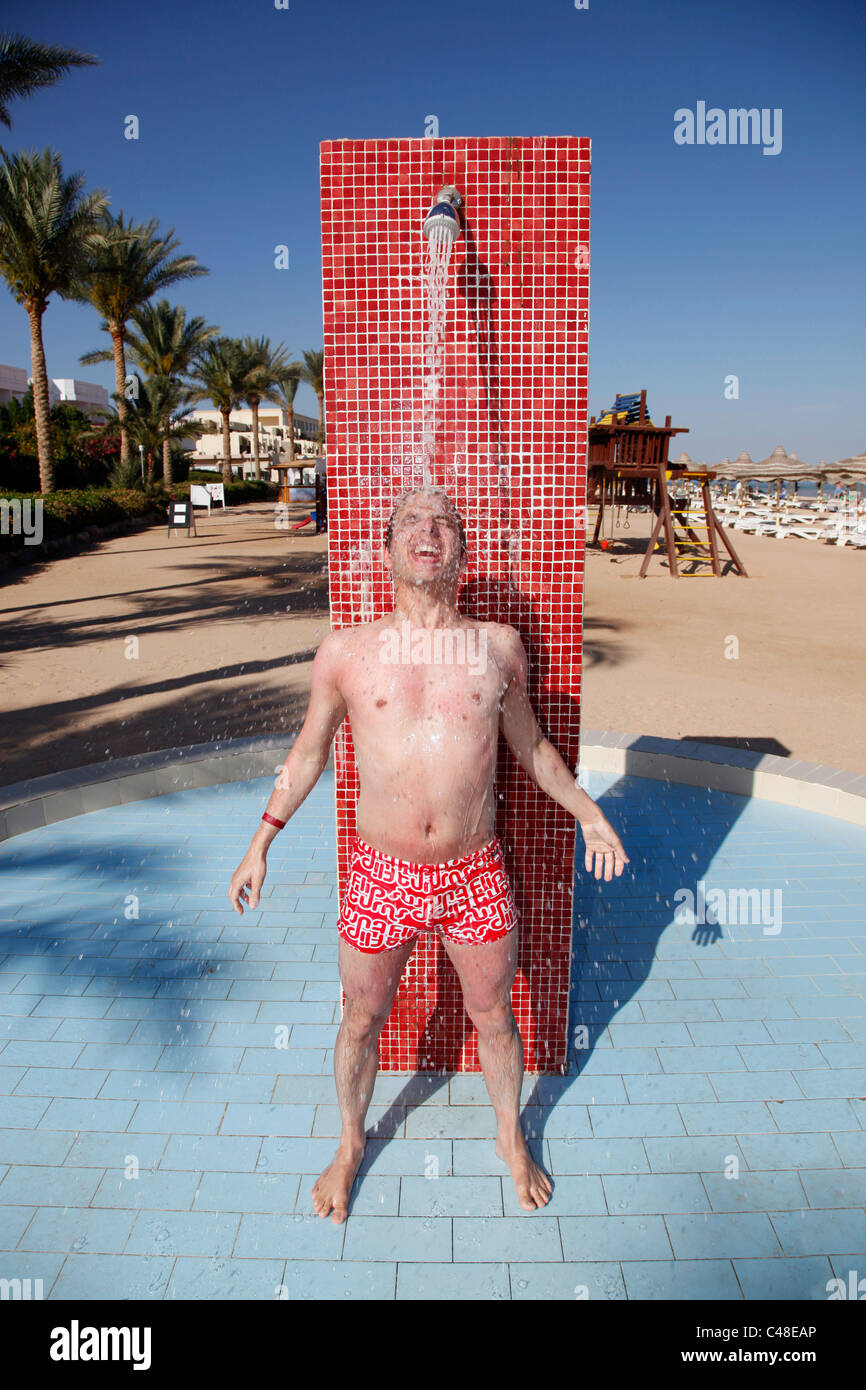 Parution du modèle homme sur des vacances lave ses cheveux sous la douche sur une plage avec les projections d'eau. Banque D'Images