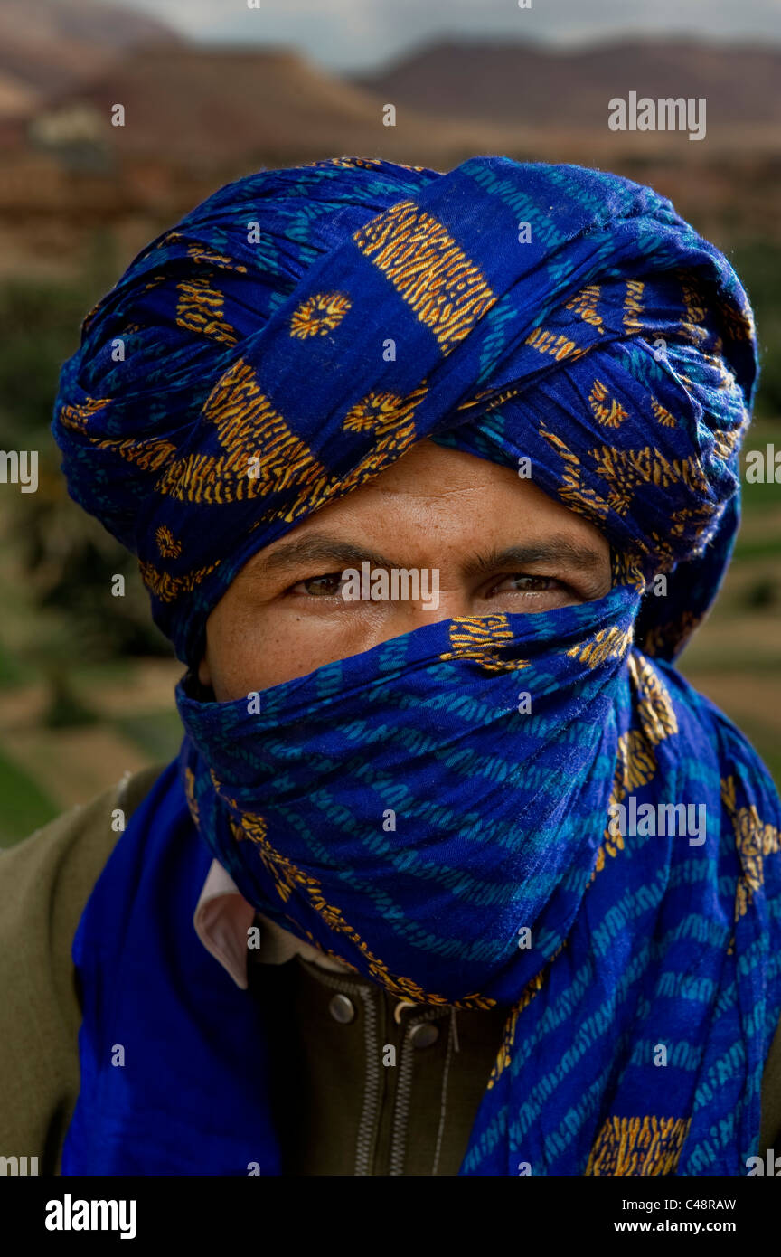Un jeune homme est assis sur le bord de la route avec son visage masqué par  un foulard bleu enroulé autour de sa tête et le visage, dans le centre du  Maroc