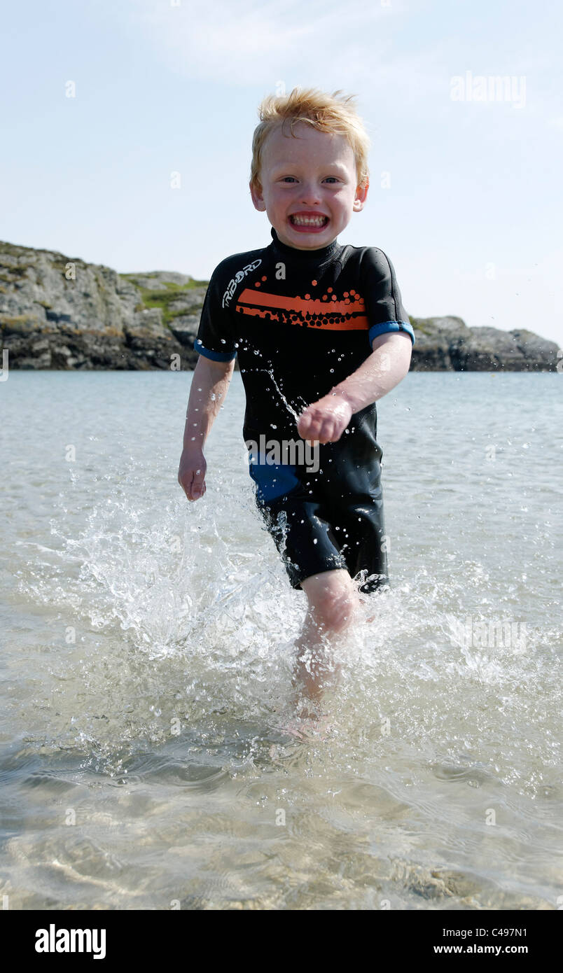 Un jeune garçon qui traverse la mer, souriant et aux éclaboussures. Banque D'Images
