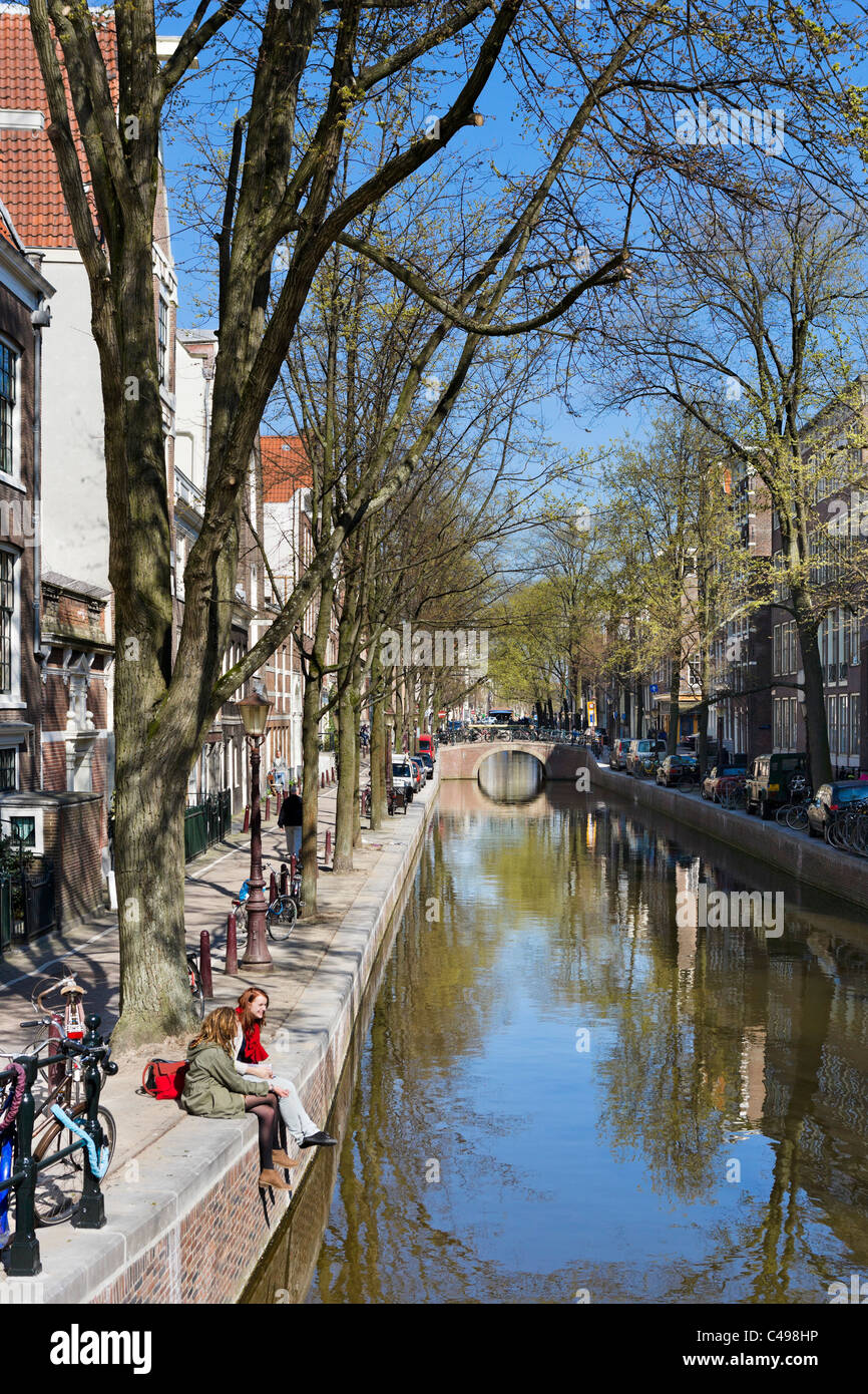 Deux jeunes femmes assises par Oudezijds Achterburgwal canal dans le Red Light District (De Wallen) au printemps, Amsterdam, Pays-Bas Banque D'Images