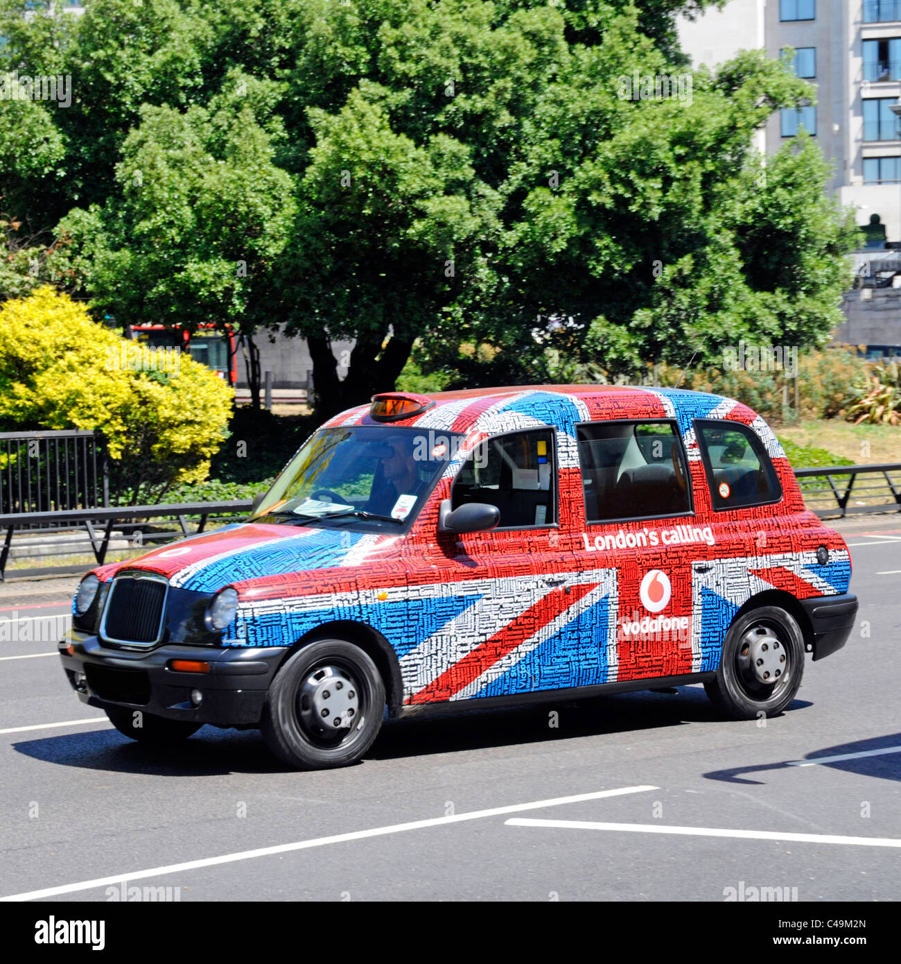 Scène de rue vue latérale noir taxi cabine temporairement couvert Vodafone London Calling Union Jack drapeau et texte tag mot nuage Graphique publicitaire Angleterre Royaume-Uni Banque D'Images