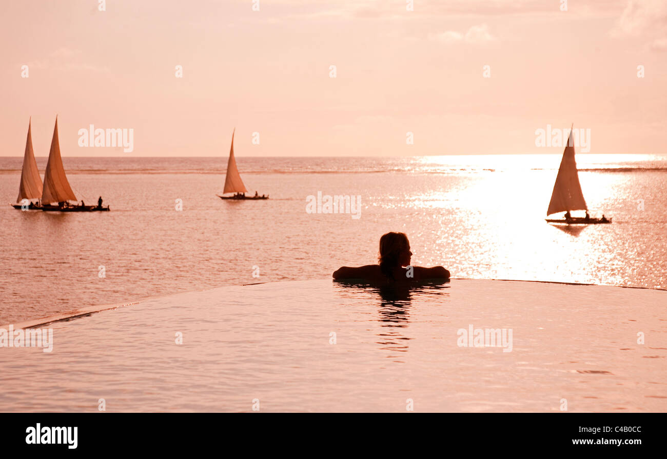 Zanzibar, Matemwe Bungalows. Un touriste se trouve au bord d'une piscine à débordement en regardant les boutres. M. Banque D'Images