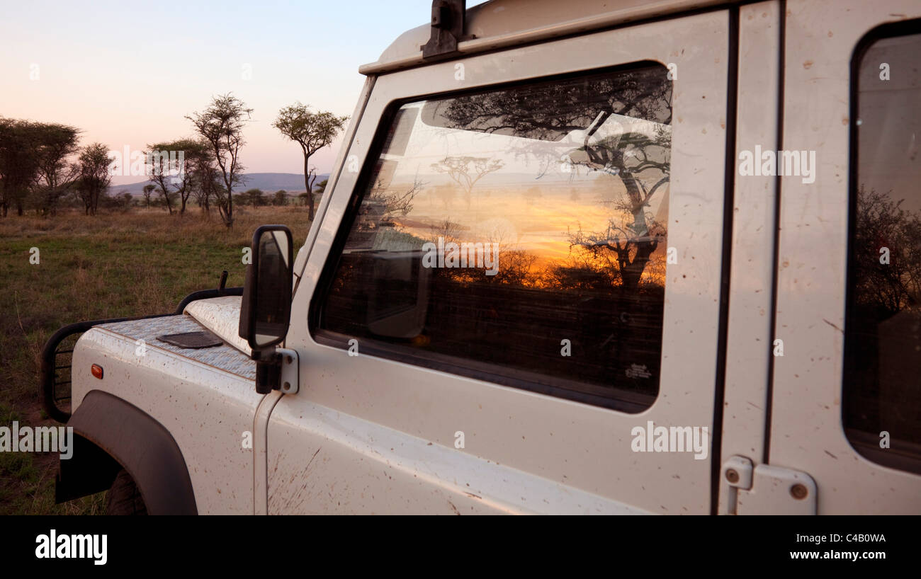 La Tanzanie, Serengeti. Lever de soleil sur la brousse se reflète dans la fenêtre d'un Land Rover. Banque D'Images
