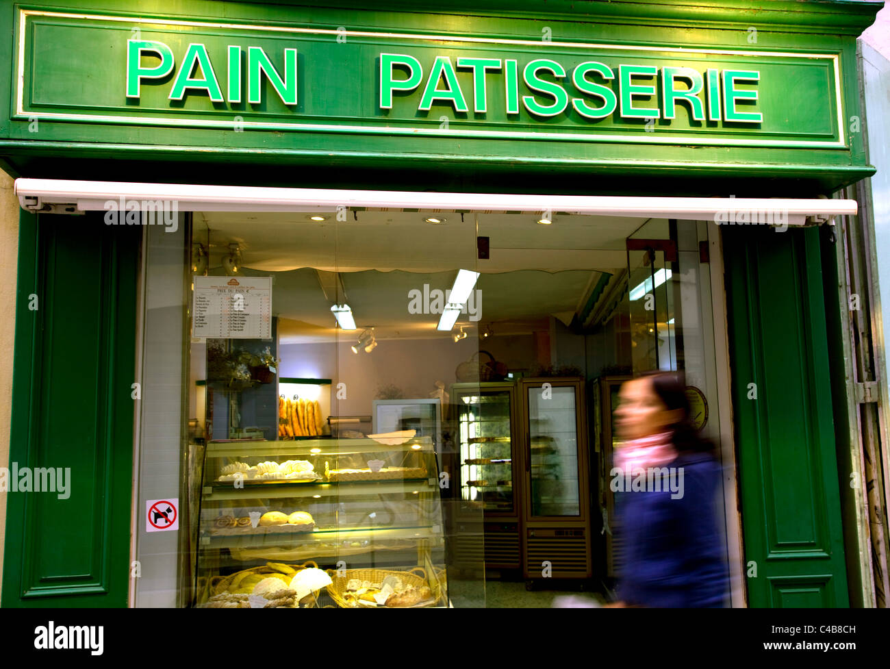 Arles, Bouches du Rhône, France ; Jeune femme marchant devant une façade de couleur vive d'une pâtisserie "douleur" Banque D'Images