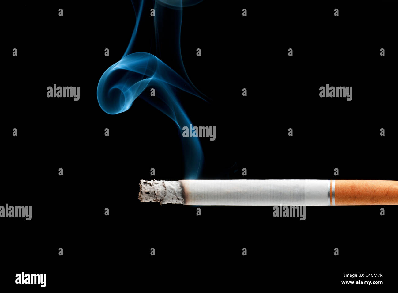 Une cigarette burning isolé sur un fond noir Banque D'Images