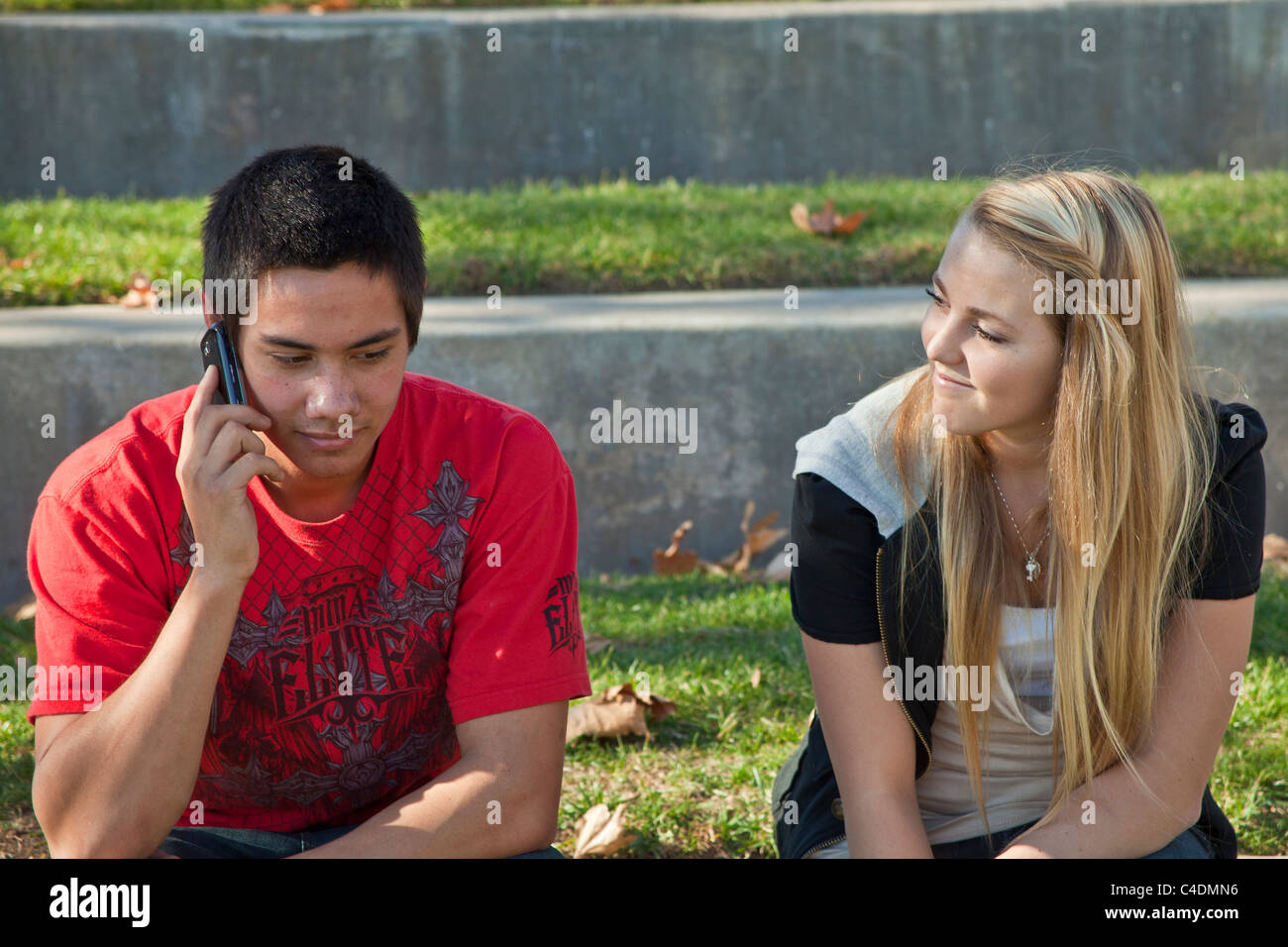 Deux jeunes de 14-16 ans une diversité ethnique raciale ethnique plusieurs adolescents parler de l'utilisation de l'iPhone téléphone mobile Américain hispanique indien Pieds-Noirs Banque D'Images
