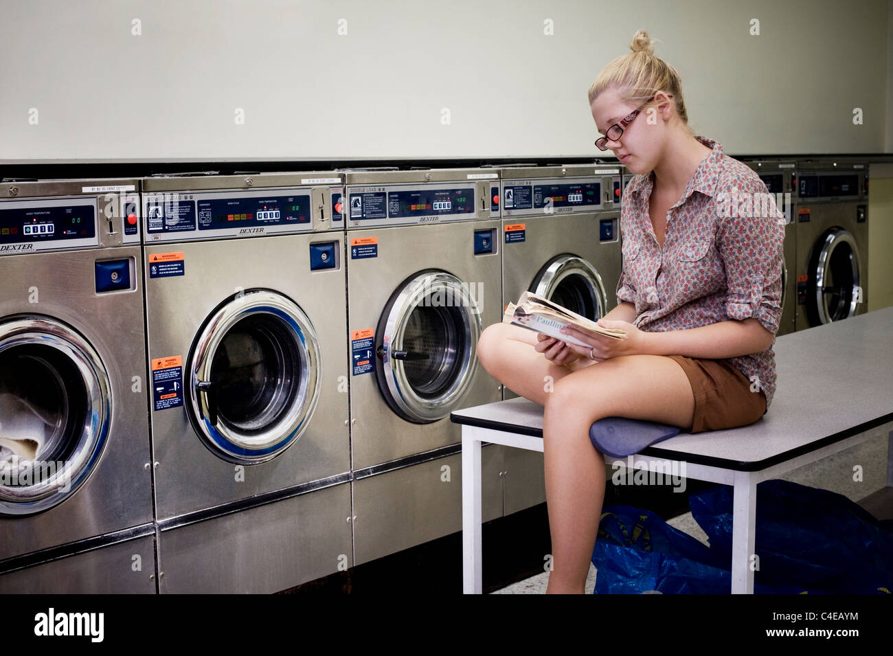 Girl reading book at laundromat Banque D'Images