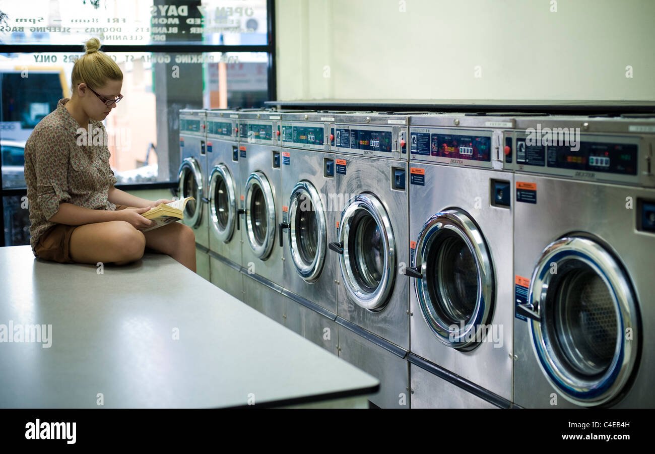 Young Woman Reading in laundromat Banque D'Images
