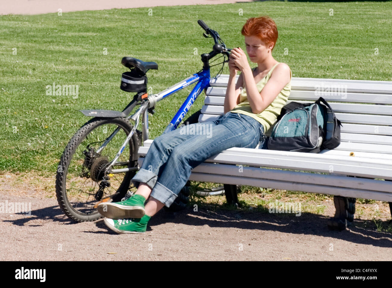 La Russie , St Petersburg , Champ de Mars War Memorial Park jolie jeune rousse sur banc de parc avec le vélo d'envoyer du texte sur téléphone cellulaire Banque D'Images