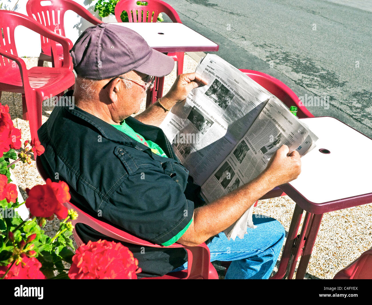 Man reading newspaper at outdoor bar / cafe table - France. Banque D'Images