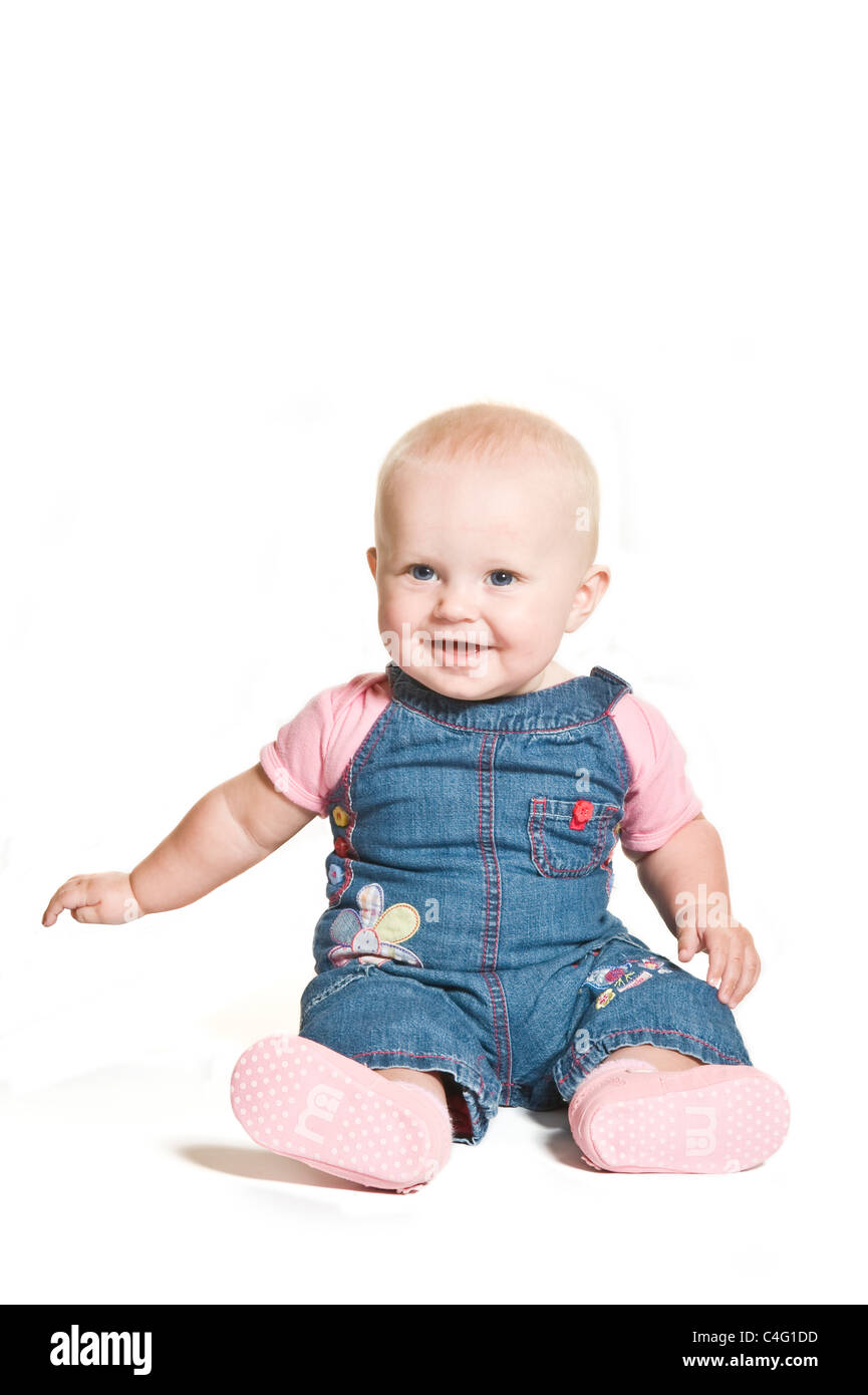 Un mignon bébé de 1 an fille aux yeux bleu denim et porter contre un sourire rose blanc pur (255) Contexte. Banque D'Images