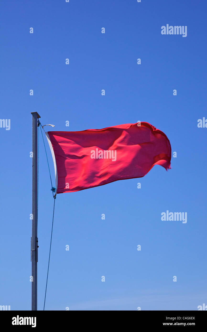 De brandir le drapeau rouge contre le ciel bleu Banque D'Images