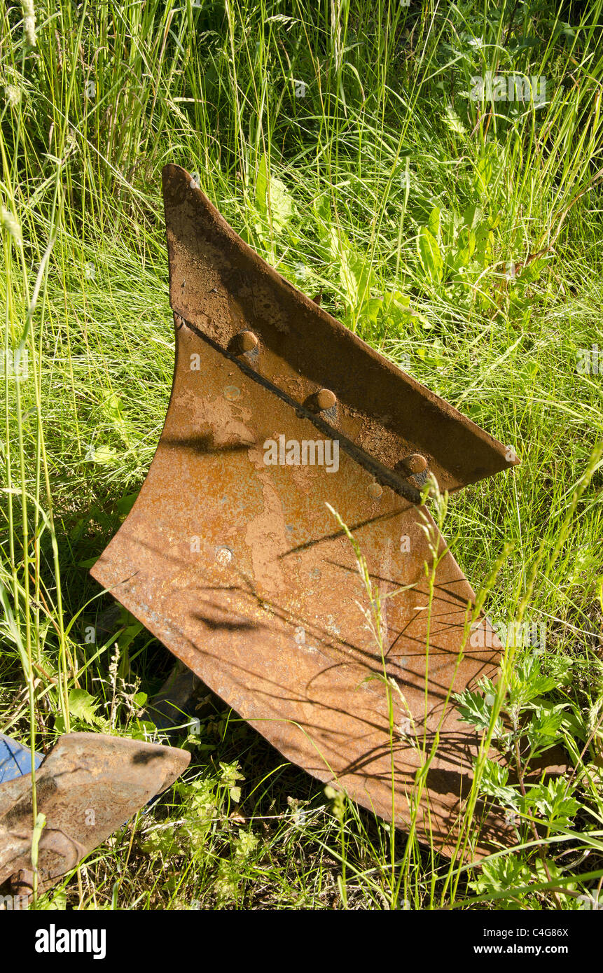 Atachable - Charrue outil agricole au tracteur pour les cultures arables. Métal rouillé dans une herbe longue. Banque D'Images