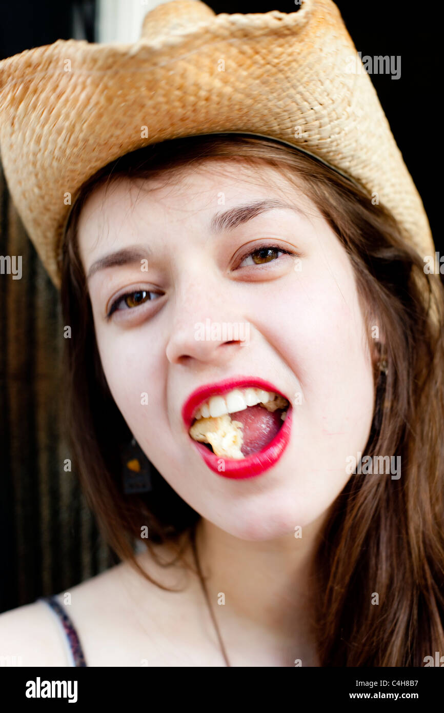 Portrait Portrait d'une jeune femme portant un chapeau et de mâcher de la nourriture avec sa bouche ouverte, London, England, UK Banque D'Images