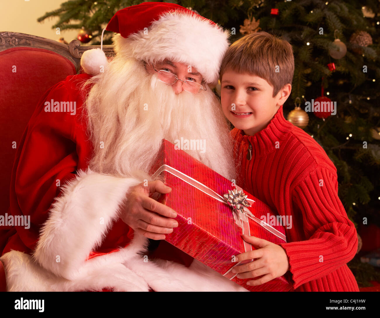 Santa Claus Giving Gift to boy in front of Christmas Tree Banque D'Images