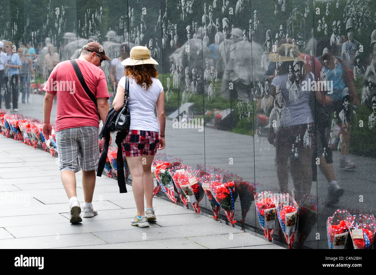 Memorial des vétérans de la guerre de Corée Reflecting Wall images gravées Washington DC // WASHINGTON DC — les visiteurs explorent le Memorial des vétérans de la guerre de Corée sur le National Mall tandis que des bouquets de fleurs bordent le mur réfléchissant en granit noir. Le mémorial présente 19 statues en acier inoxydable représentant des membres du service militaire américain. Le mur, qui s'étend sur 164 pieds de long, affiche des images photographiques de la guerre de Corée gravées dans sa surface. Banque D'Images
