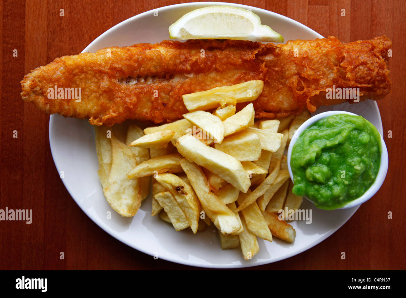 Un plat de poisson et frites est servi avec des petits pois et une pointe de citron. Banque D'Images