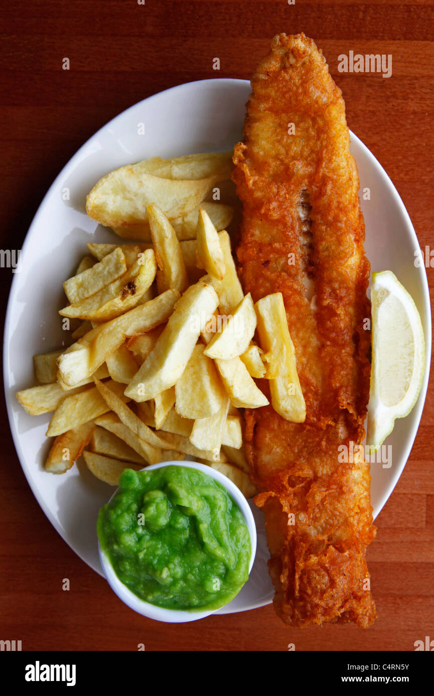 Un plat de poisson et frites est servi avec des petits pois et une pointe de citron. Banque D'Images