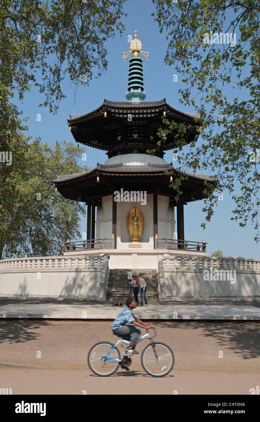 Un jeune cycliste en passant en face de la Pagode de la paix bouddhiste japonaise, Battersea Park, London, UK. Banque D'Images