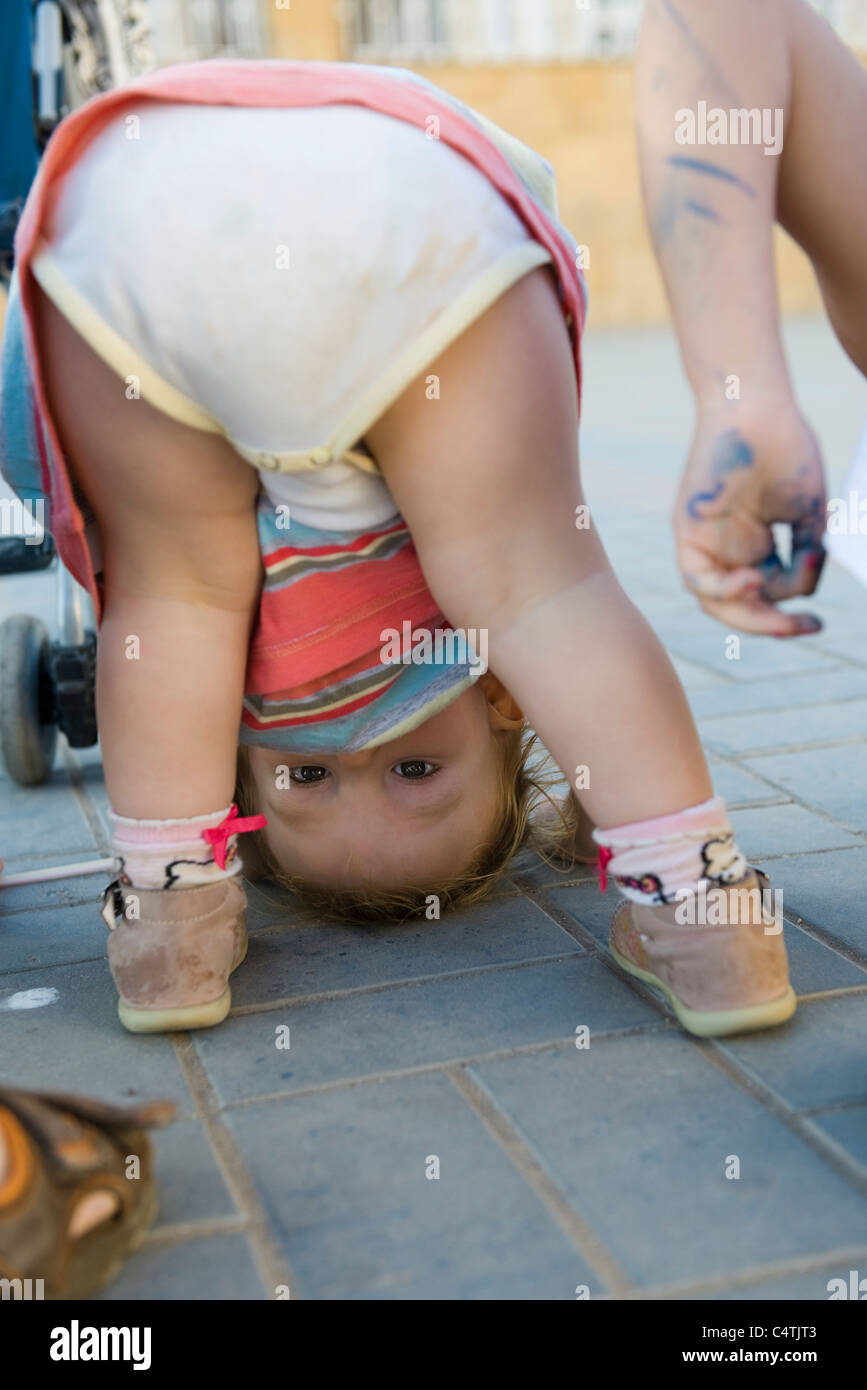 Bébé fille se pencher, peeking through jambes at camera Banque D'Images
