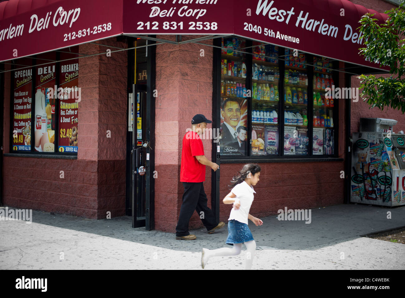 Un homme et de la jeune fille passer une photographie du président Barack Obama et le président John F. Kennedy dans la fenêtre d'une épicerie à Harlem Banque D'Images