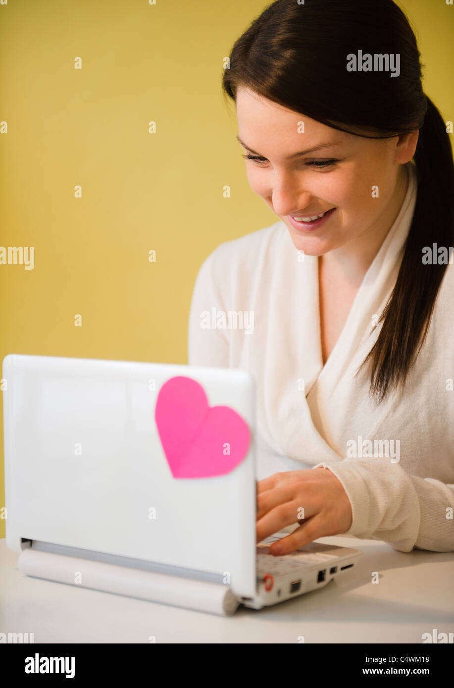 Smiling young woman using laptop avec coeur rose Banque D'Images