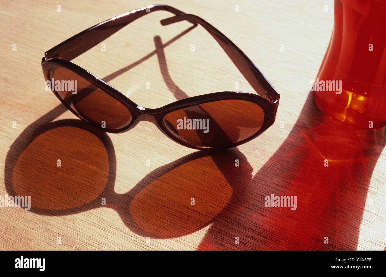 Lunettes de soleil et tumbler sur rouge à grain du bois de la table et d'ombres colorées Banque D'Images Lunettes de soleil et tumbler sur rouge à grain du bois de la table et d'ombres colorées Banque D'Images
