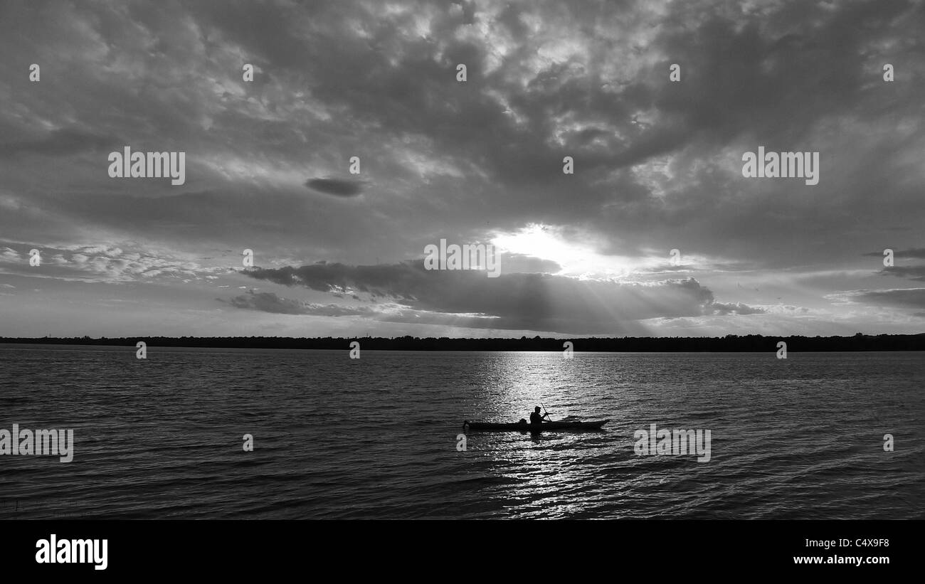 Kayak solitaire qui se découpent sur le pittoresque lac au coucher du soleil. Banque D'Images