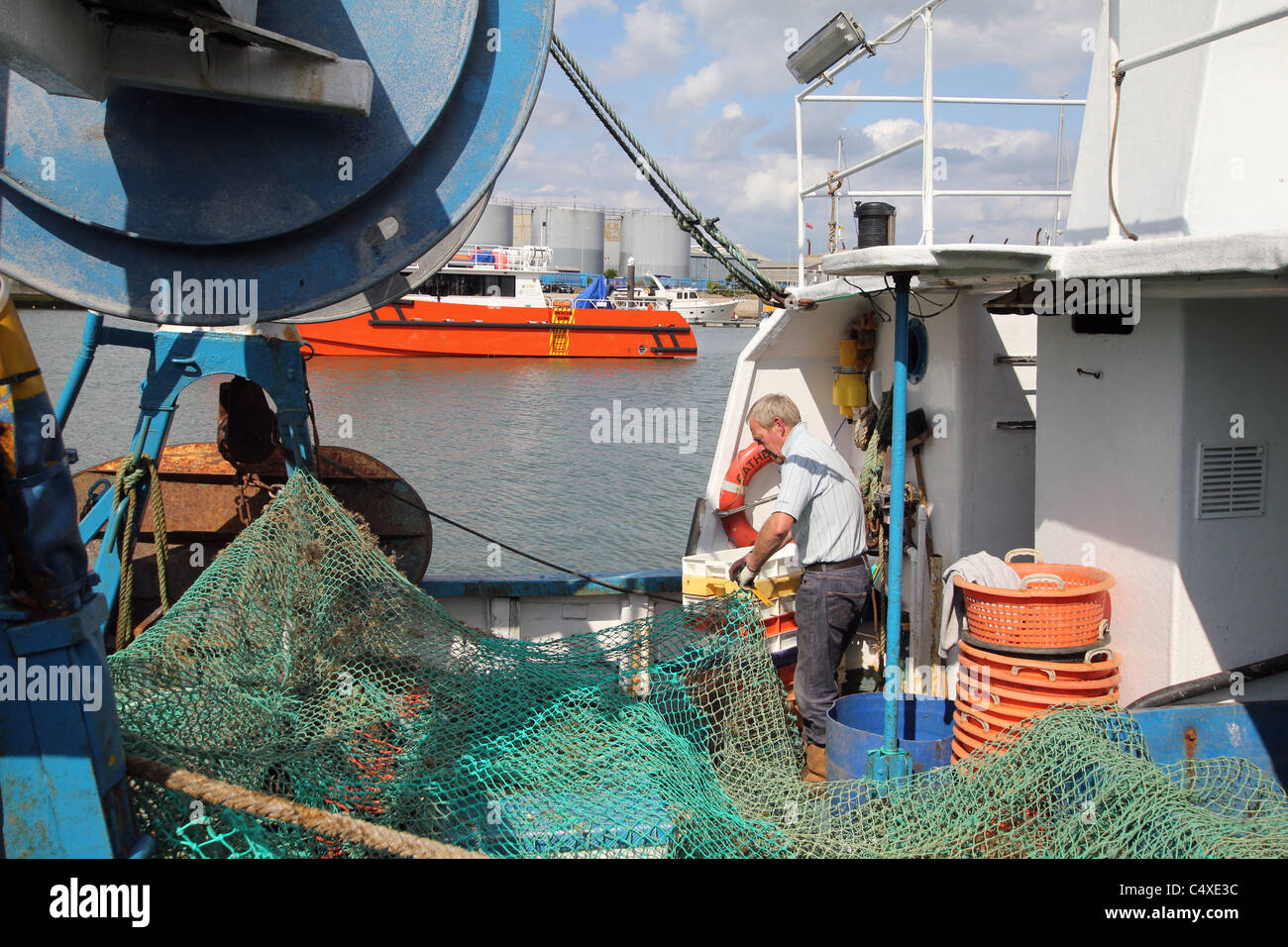 Un pêcheur réparant son filet à l'arrière de son bateau. Banque D'Images