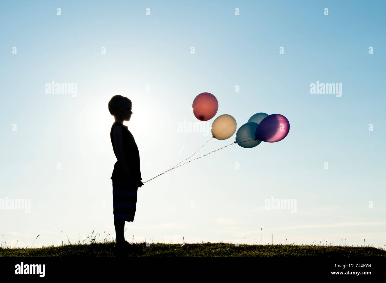 Silhouette d'un jeune garçon tenant des ballons de couleur au coucher du soleil Banque D'Images