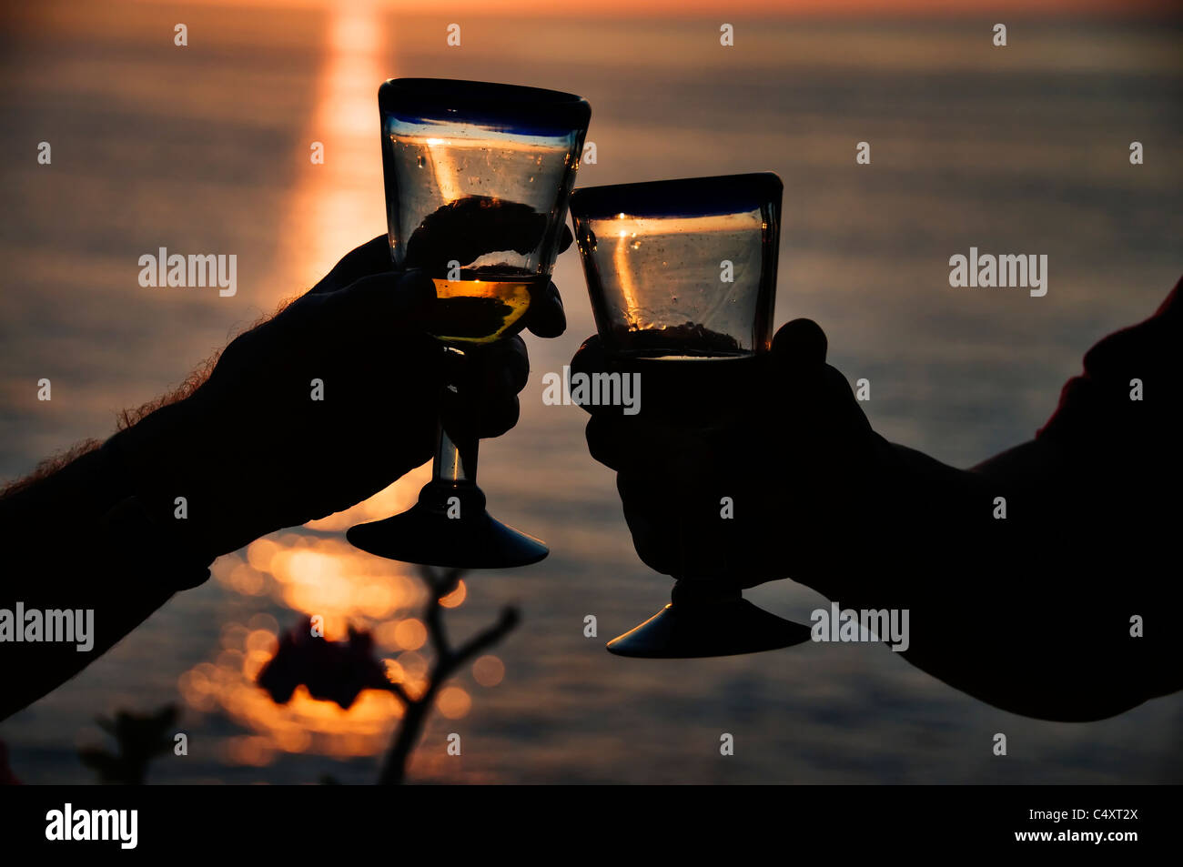Deux hommes faire un toast au coucher du soleil avec des verres à vin soufflé à la main donnant sur l'océan Pacifique à San Pancho, le Mexique. Banque D'Images