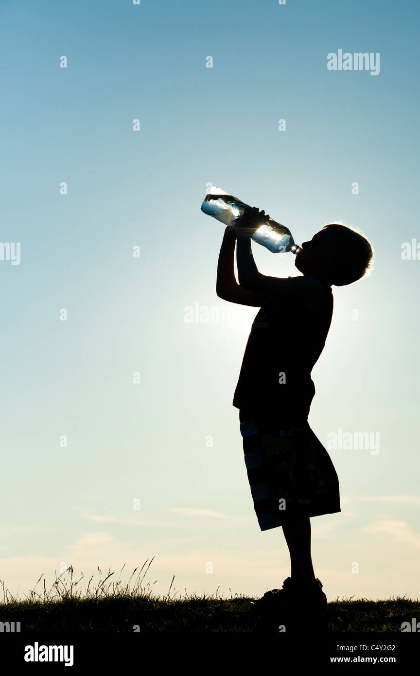 Boy boire de l'eau minérale à partir de la bouteille d'eau en plastique. Silhouette Banque D'Images