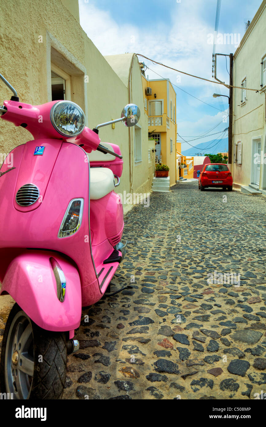 Typique de Santorin île grecque iconique scooter rose sur la rue pavée à Thira voiture rouge Banque D'Images