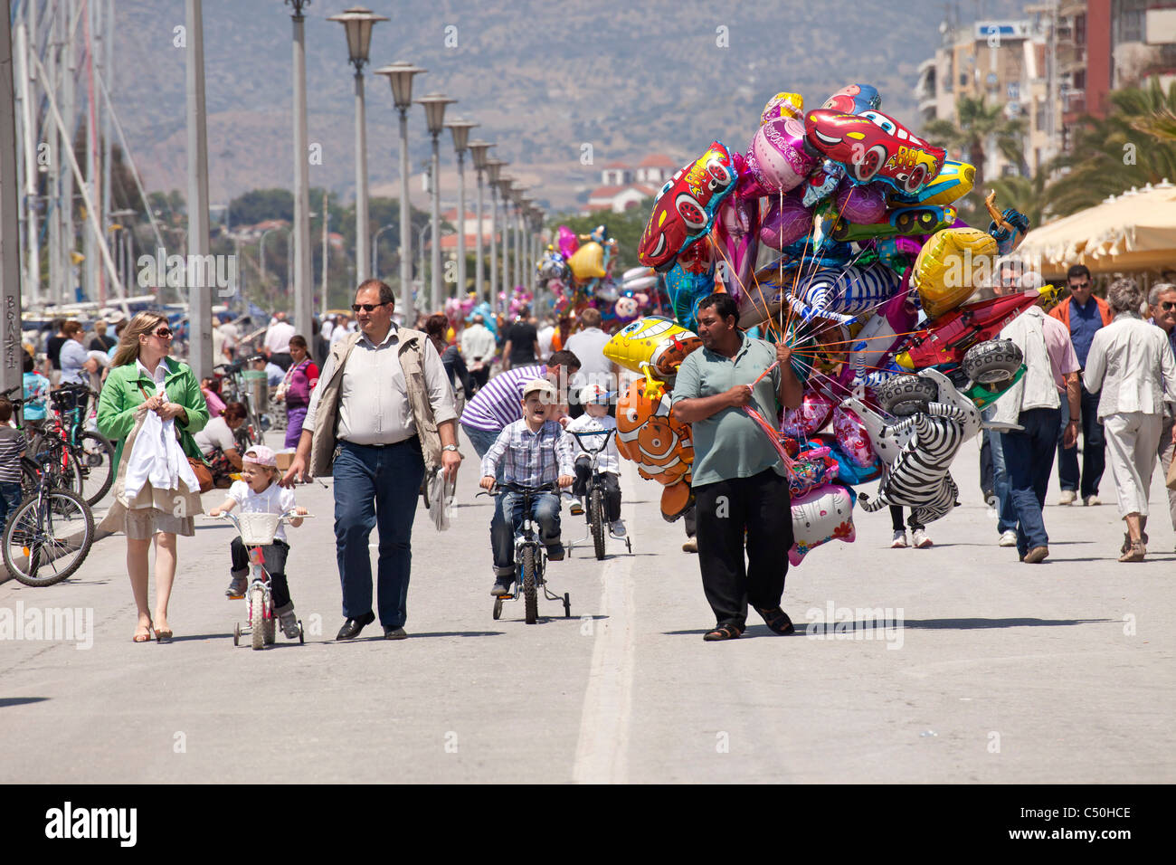 Vendeur de ballons et les enfants sur des vélos sur la promenade du port de la ville portuaire côtière, Volos Thessalie, Grèce Banque D'Images