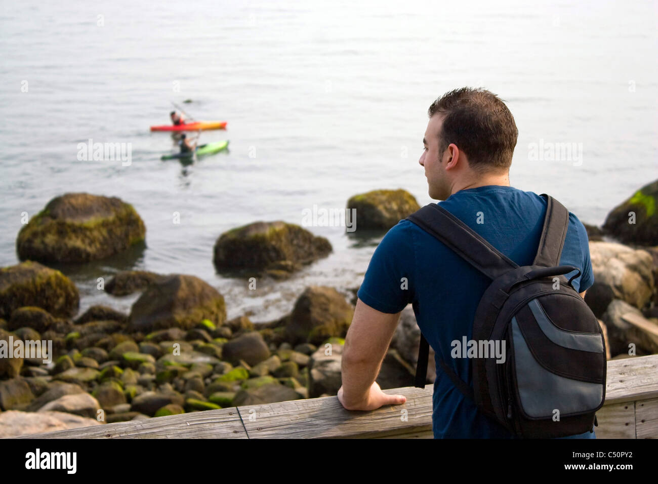 Un jeune homme jouit de la vue par la mer que deux personnes kayak dans la distance. Profondeur de champ. Banque D'Images