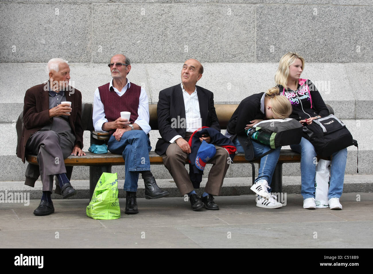 5 personnes assises sur un banc, une avec sa tête posée sur son sac à dos. A lieu à Trafalgar Square, Londres Banque D'Images