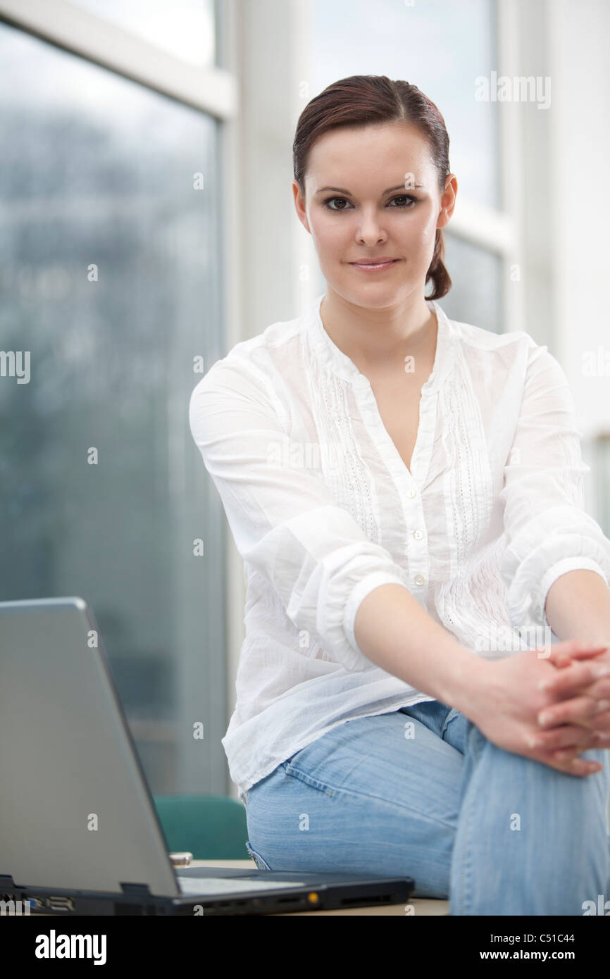 Portrait of young businesswoman sitting on desk Banque D'Images