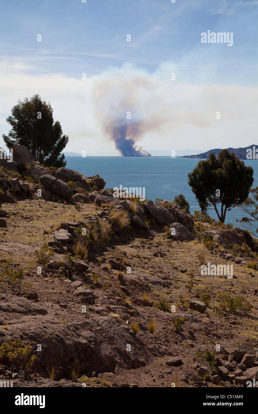 Vue depuis l'île de Taquile combustion illégale de roseaux, le Lac Titicaca, Pérou Banque D'Images