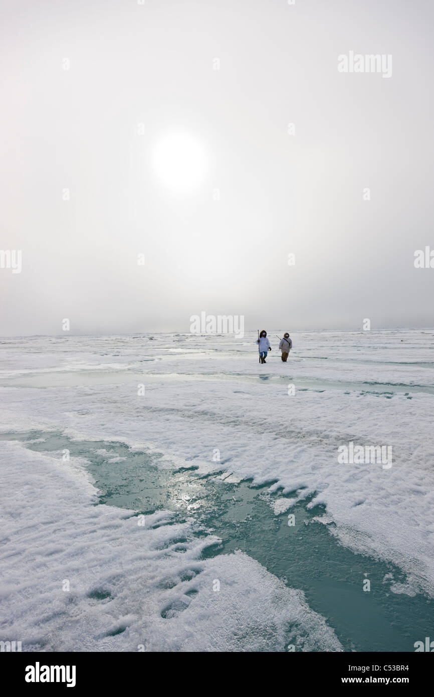 Les chasseurs esquimaux Inupiaq transporter un fusil et bâton de marche en marchant sur la glace de rive le long de la mer de Tchoukotka, Barrow, Alaska Banque D'Images