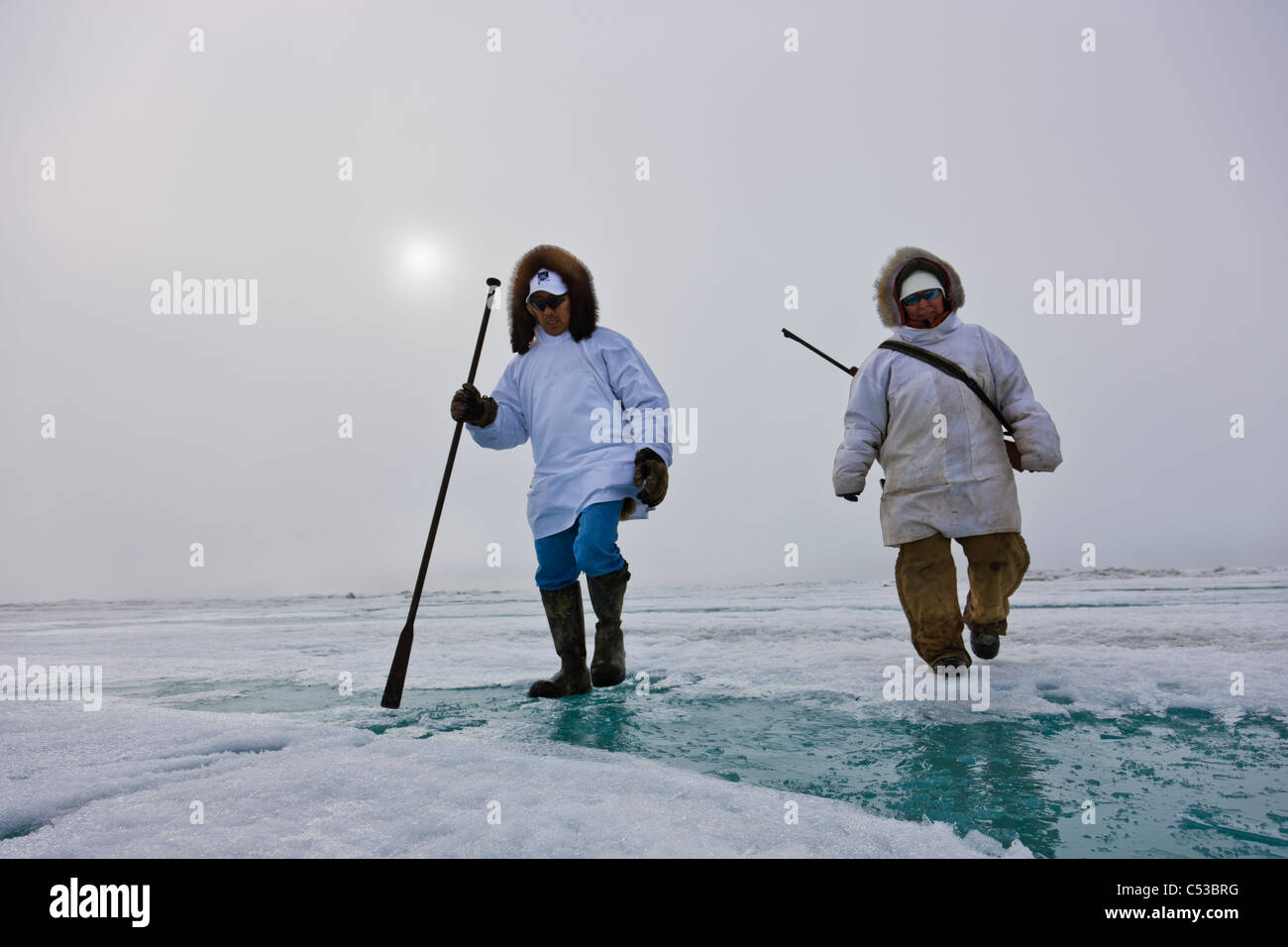 Les chasseurs esquimaux Inupiaq transporter un fusil et bâton de marche en marchant sur la glace de rive le long de la mer de Tchoukotka, Barrow, Alaska Banque D'Images
