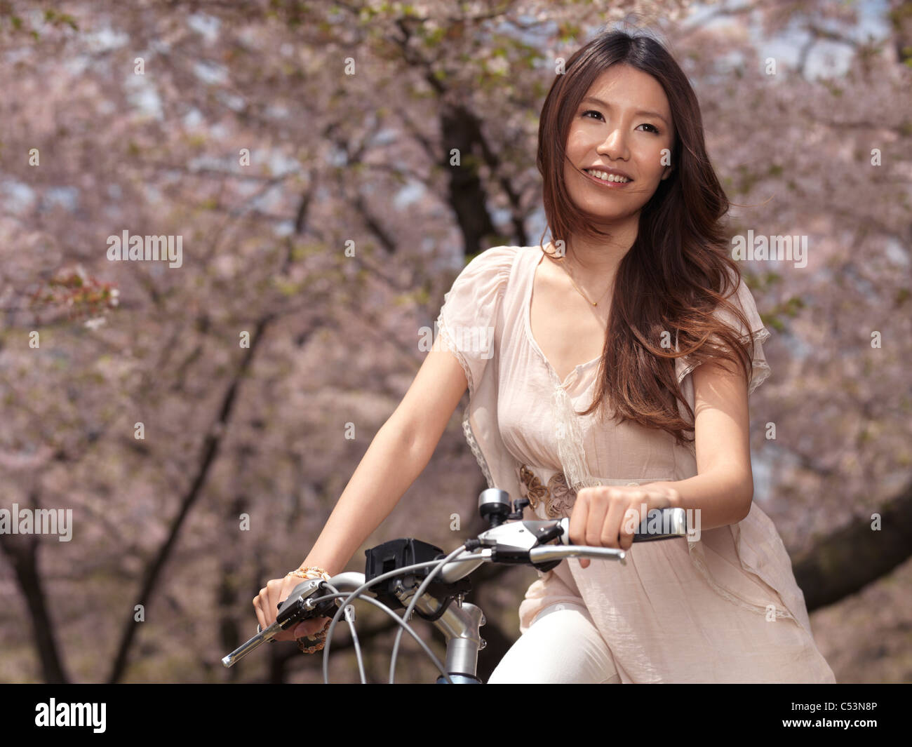 Young smiling woman sitting in a park passé cerisiers en fleurs Banque D'Images