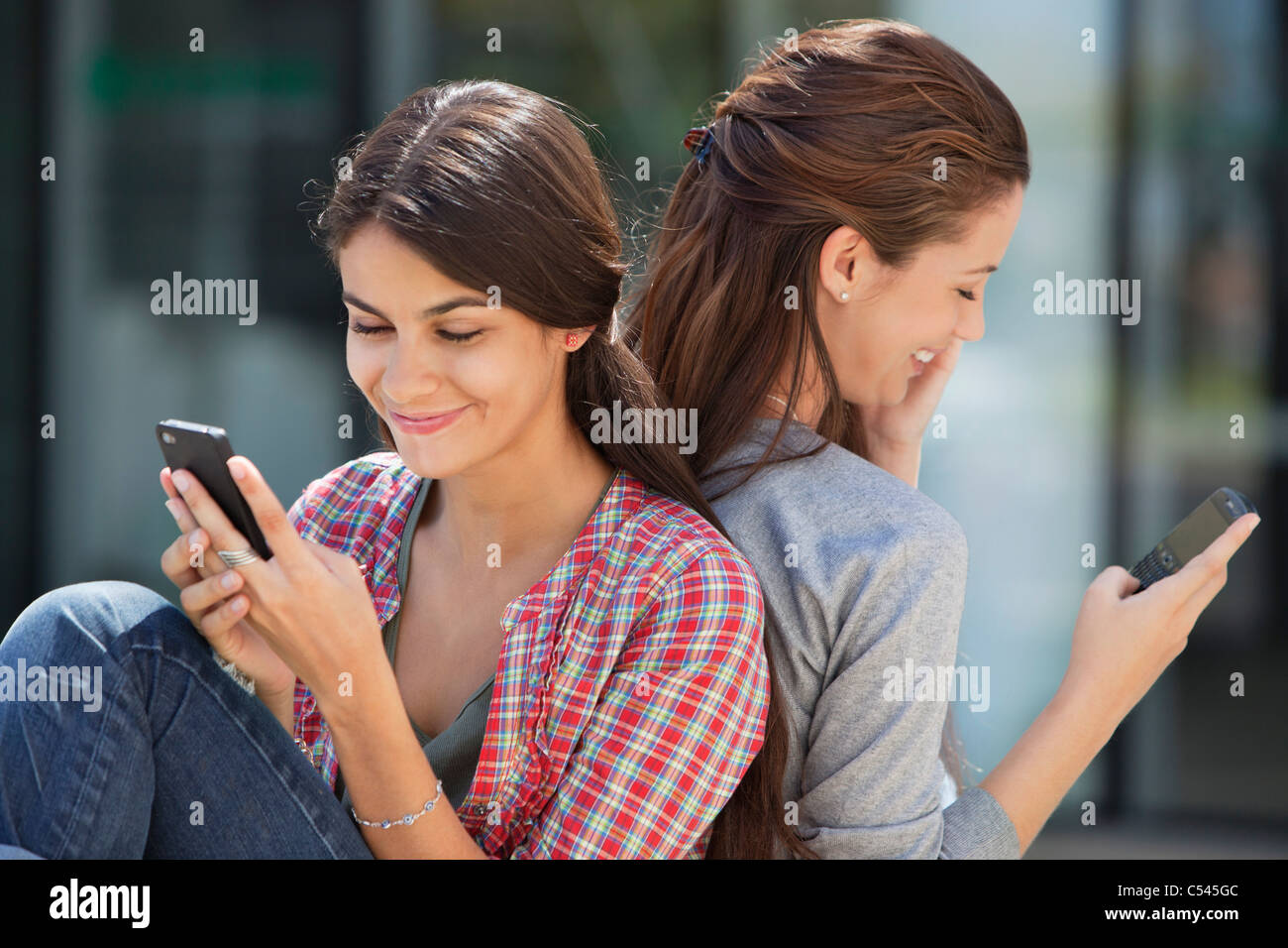 Deux jeunes femmes assis dos à dos et de messagerie texte Banque D'Images