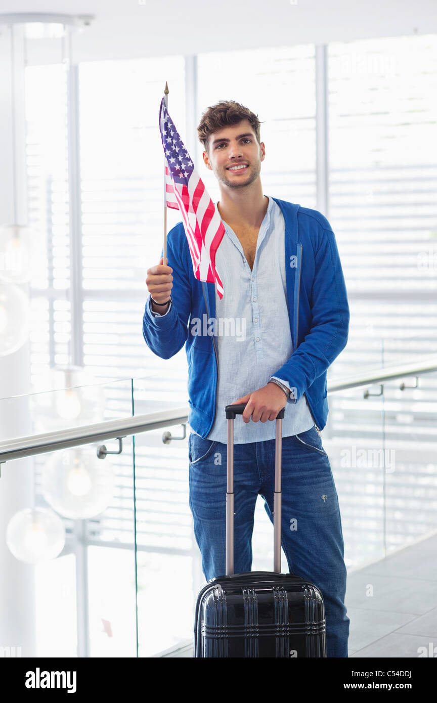 Portrait d'un homme tenant un drapeau américain et d'une valise dans un aéroport Banque D'Images