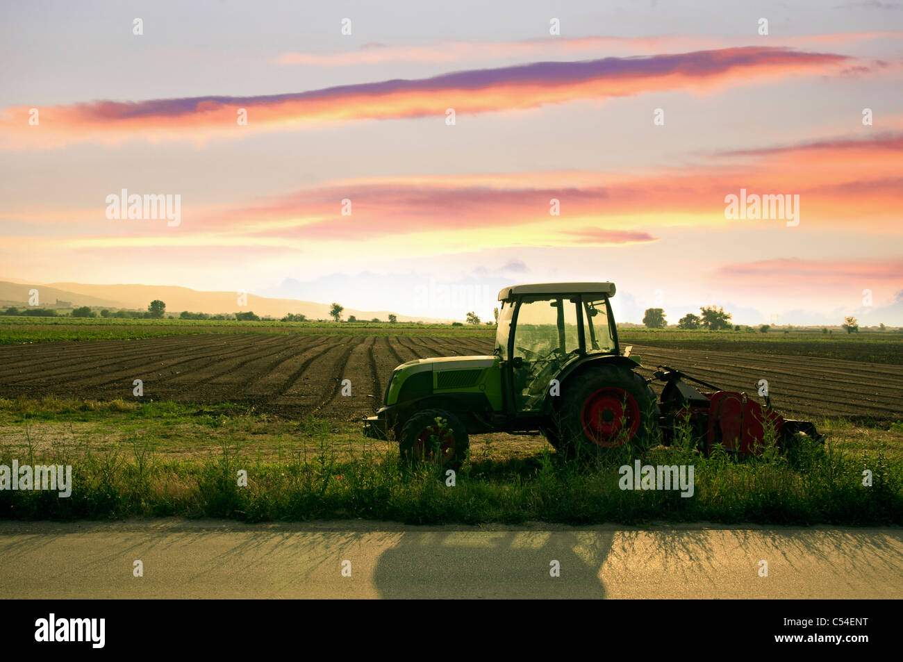 Terre labourée et le tracteur sur le coucher du soleil Banque D'Images