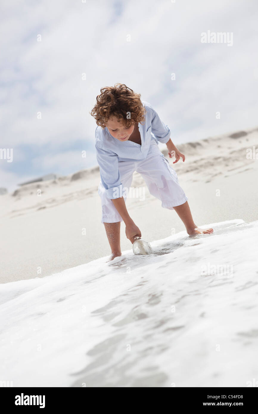 Boy putting bouteille avec message dans de l'eau sur plage Banque D'Images