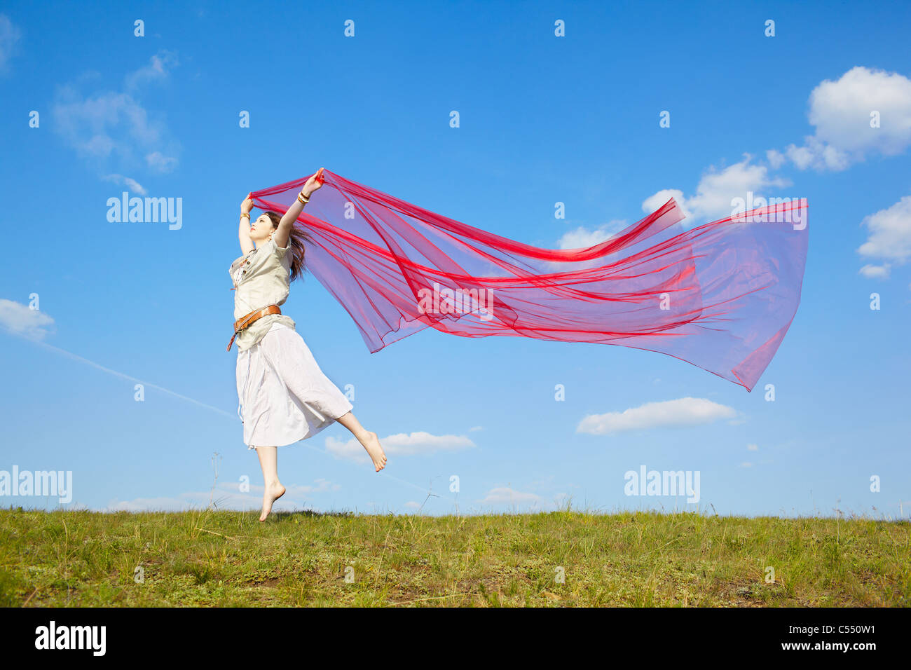 Portrait plein air de belle fille hippie sautant avec gros morceau de tissu rouge sous le ciel bleu Banque D'Images