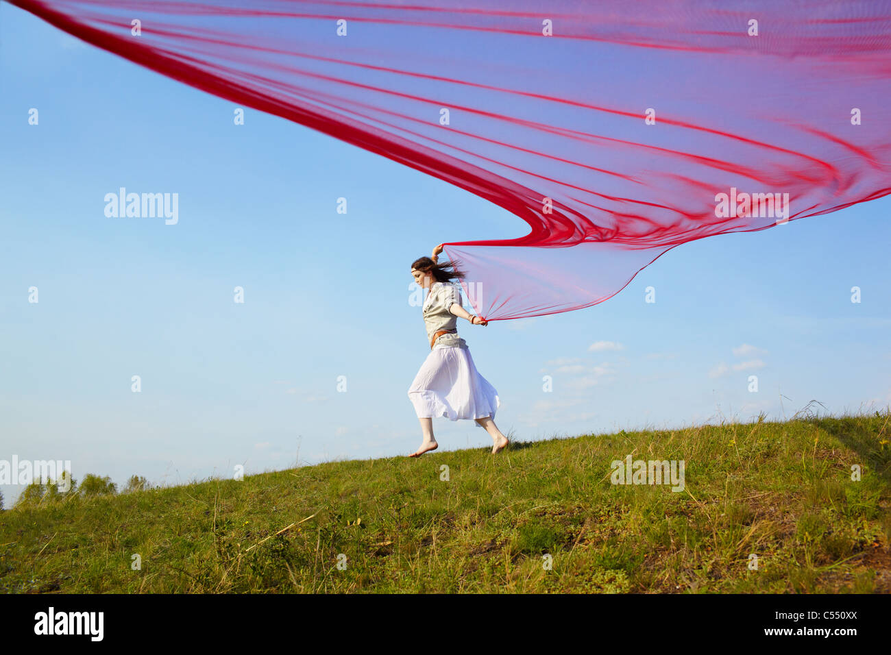 Portrait plein air de belle fille hippie fonctionnant avec de gros morceau de tissu rouge sous le ciel bleu Banque D'Images
