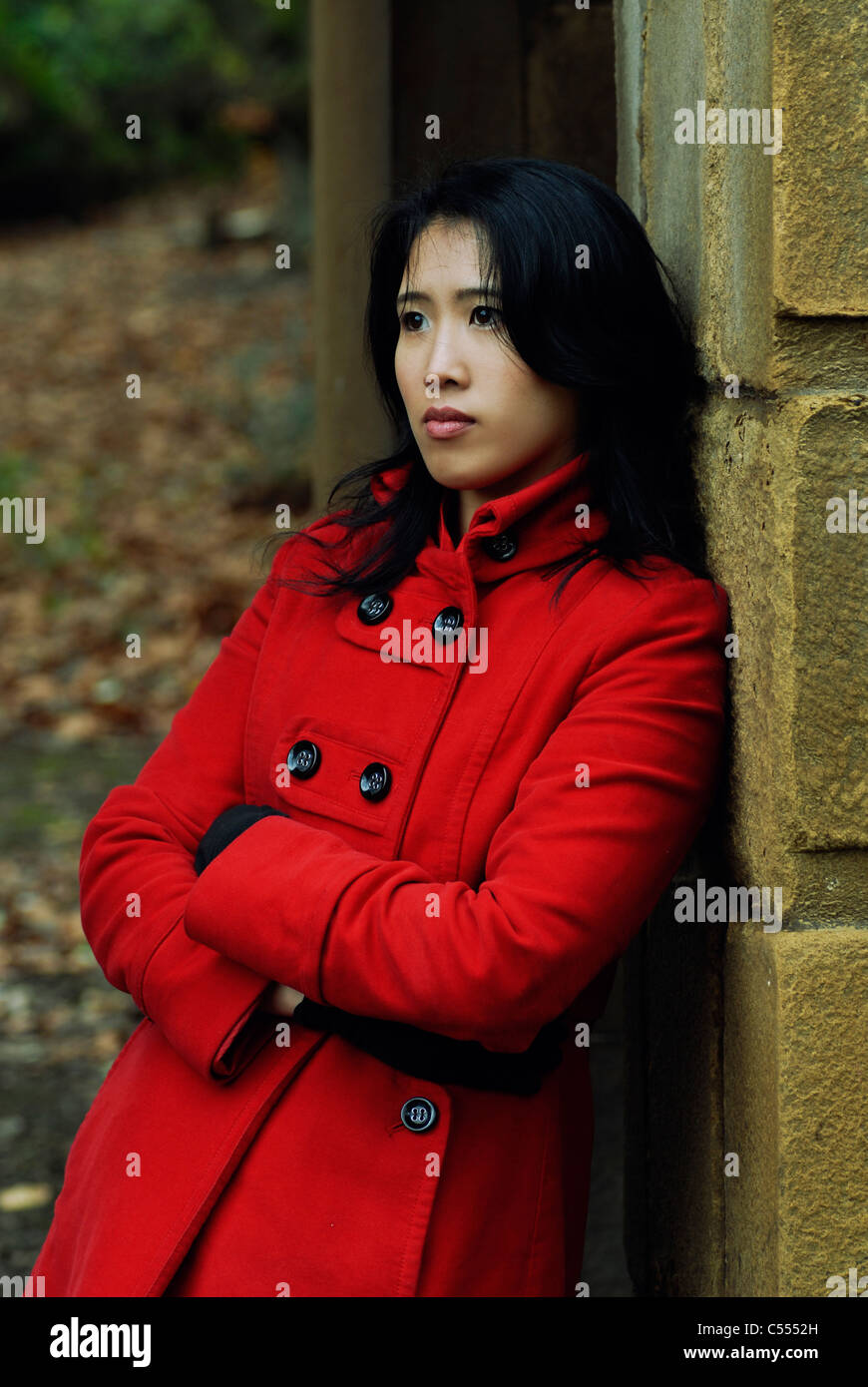 Young Chinese woman standing outdoors in red coat looking away Banque D'Images