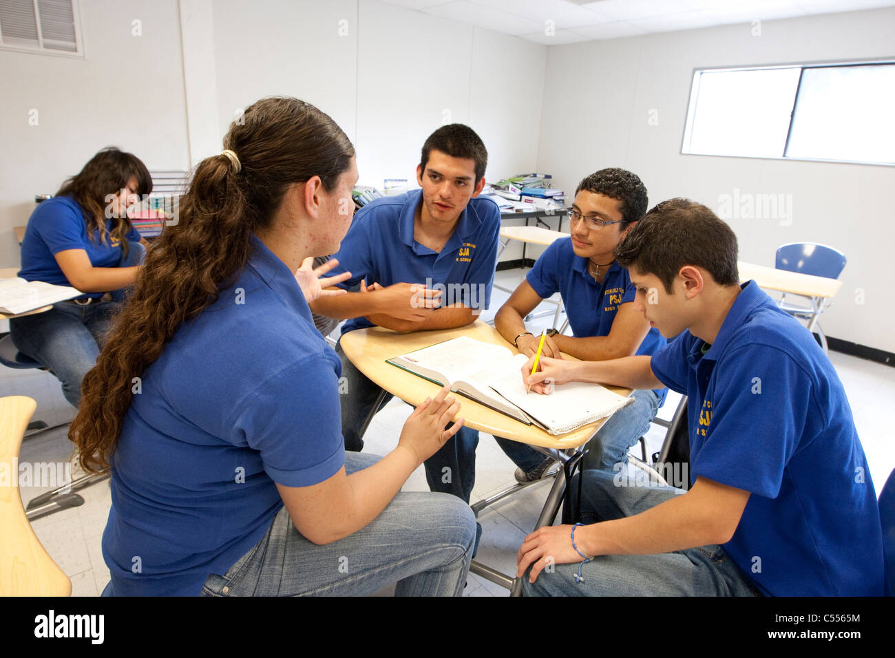 Groupe d'hommes femmes hispaniques les élèves portent des uniformes polo bleu se rassemblent autour de 24 pour discuter du projet de l'école à l'école secondaire Banque D'Images